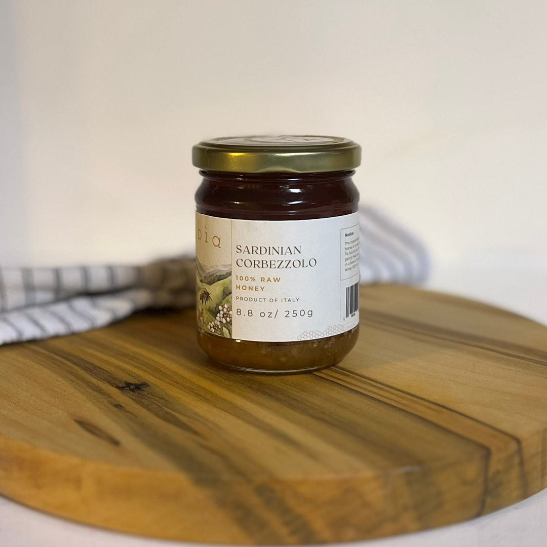 Jar of Sardinian Corbezzolo honey on a wooden board with a white background